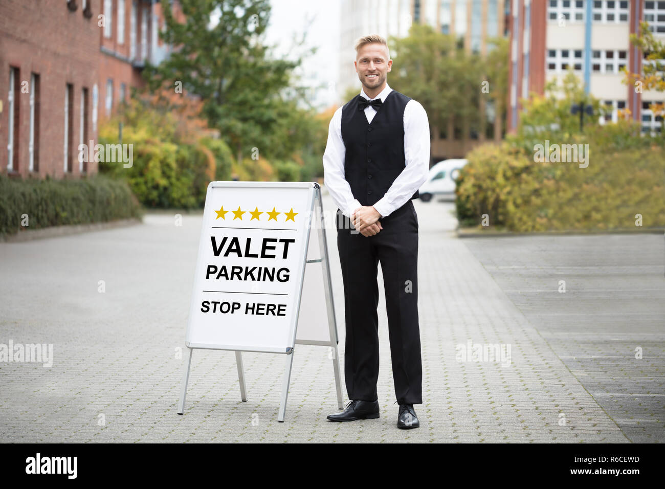 young-male-valet-standing-near-valet-parking-sign-R6CEWD.jpg